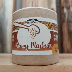 Pot de Curry Madras de la marque MeiBon – Mélange d’épices conditionné en tube carton recyclable de 50 g, posé sur une table en bois, avec une étiquette colorée et illustrée d’une cuillère à épices.